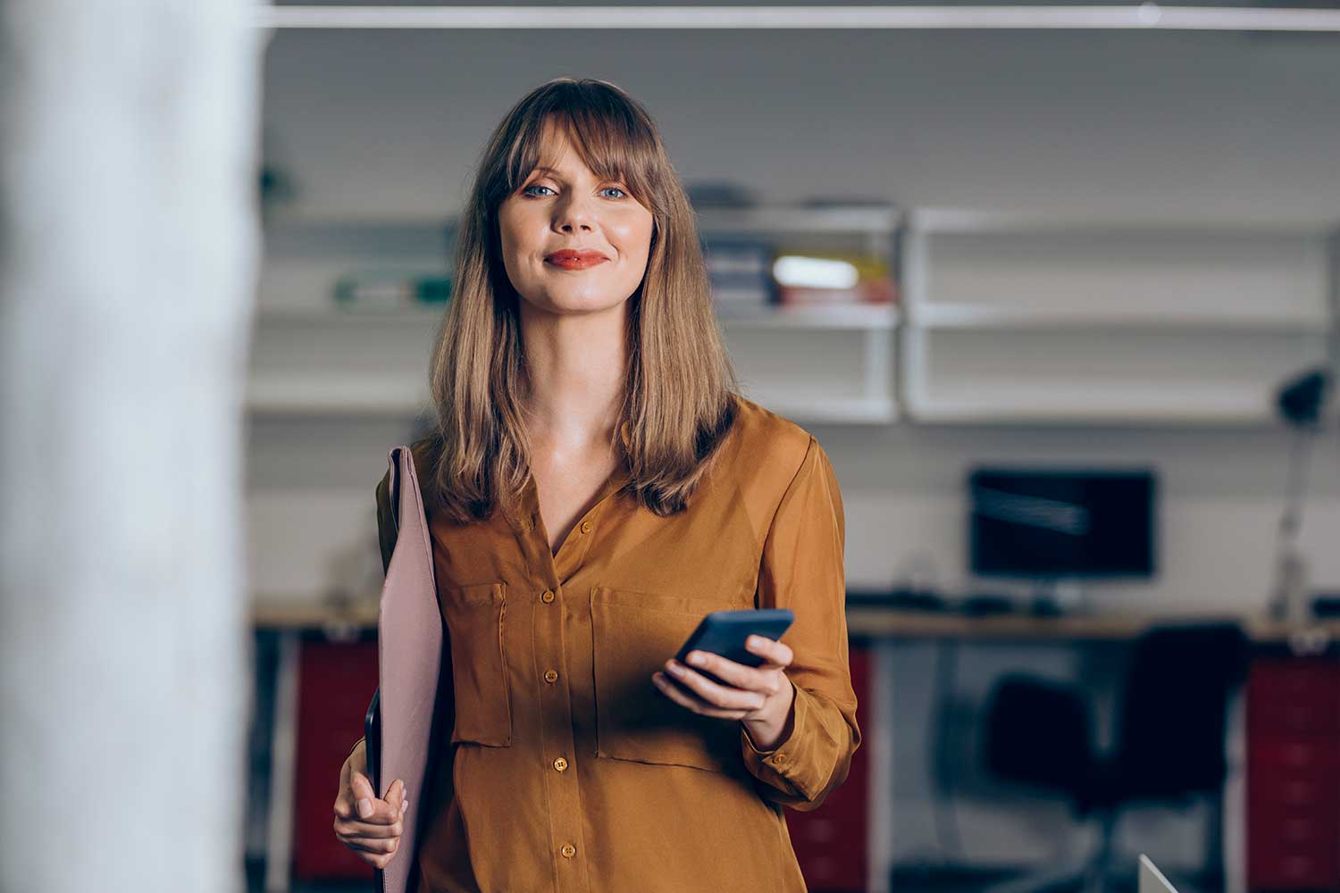 Woman in office holding phone and looking ahead